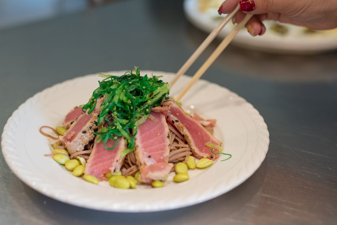Seared ahi tuna and wakame salad over buckwheat noodles and edamame, with chopsticks lifting a bite
