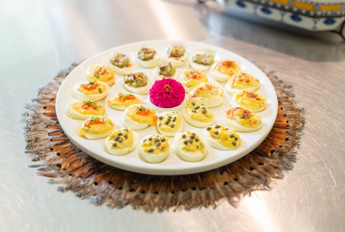 A platter of deviled eggs in several flavors, with a pink flower at the center