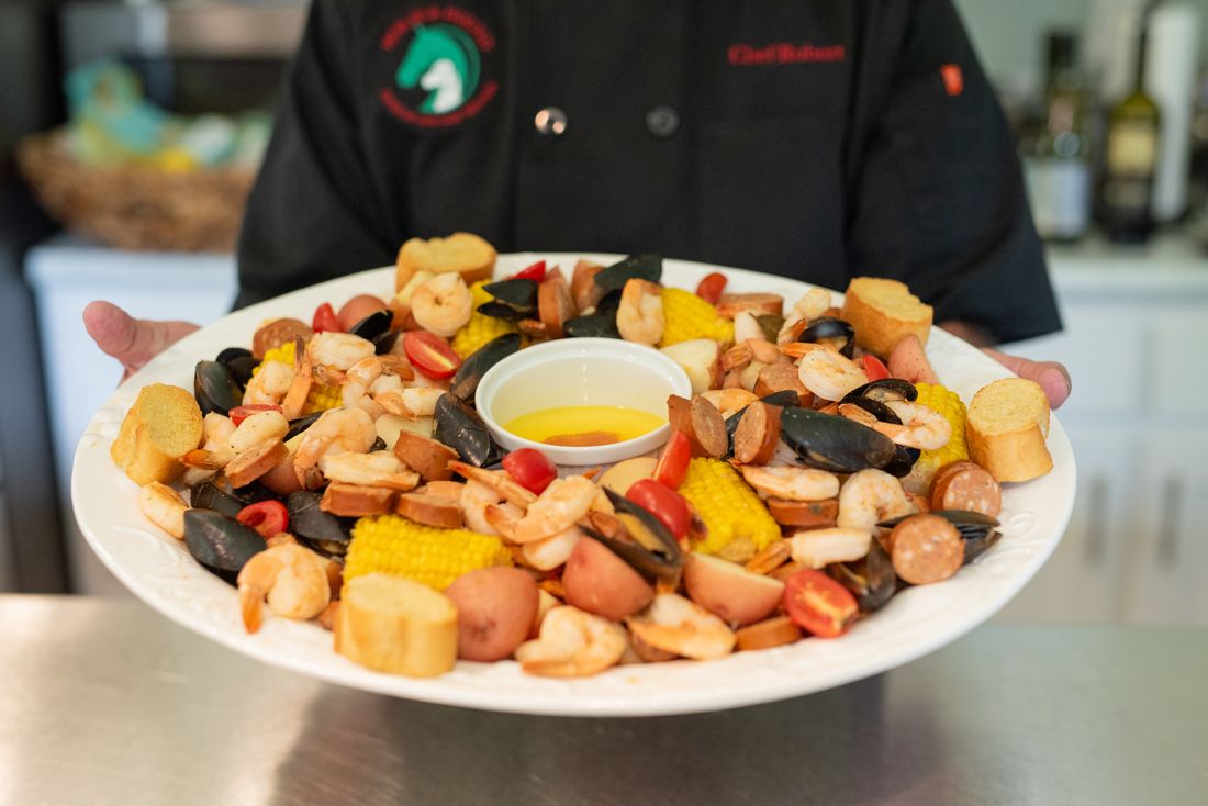 Chef Robert holding a platter of shrimp, sausage, corn, potatoes and mussels