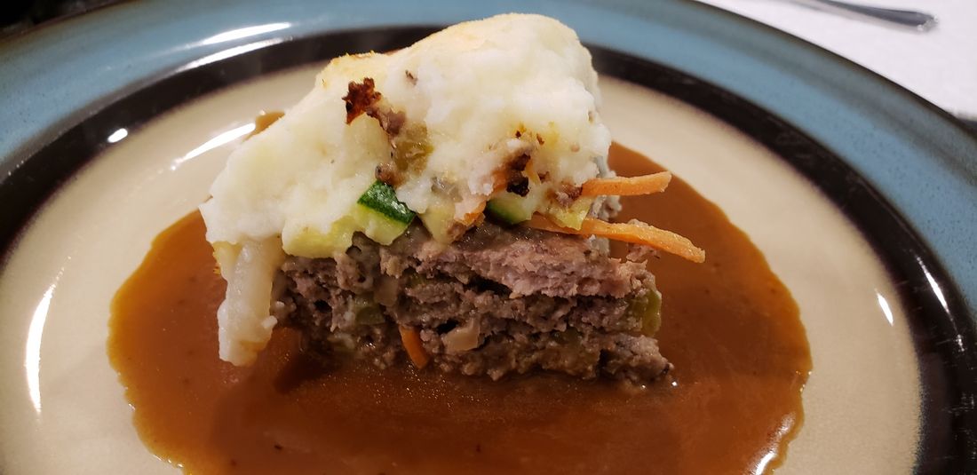 A slice of shepherd's pie topped with mashed potatoes, served over gravy